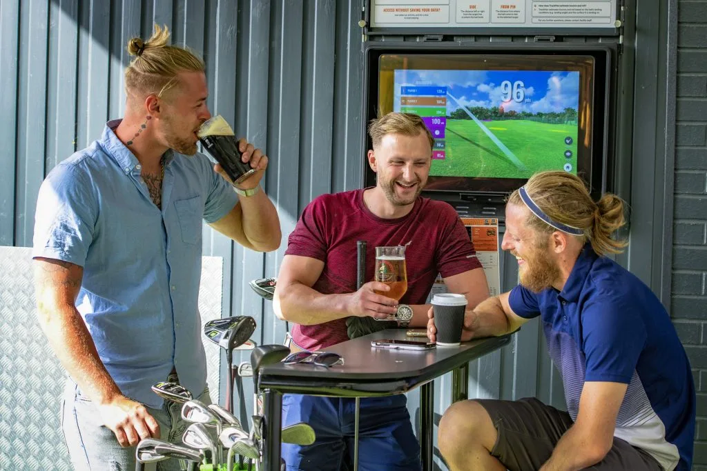 group of golfers laughing with drinks at trackman driving range in dartford