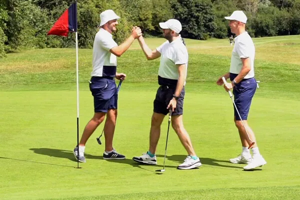 3 male golfers celebrating with each other on green at golf club in dartford