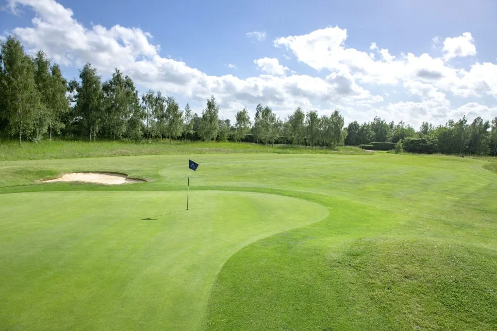Golf green with flag and bunker under blue skies at Birchwood Golf and Country Club